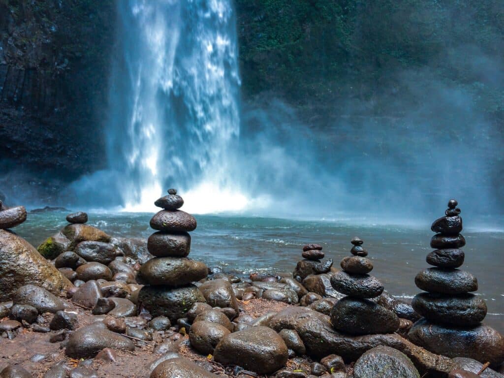 Stacked stones for meditation in front of a blue waterfall in the jungle