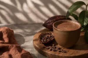 bebida caliente de cacao puro en taza de cerámica con nibs de cacao y vaina de cacao sobre fondo de madera
